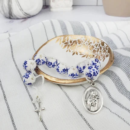 Blue and white floral sacrifice beads sitting in a clay dish with gold details. A medal of St. Therese is visible on one end and a crucifix on the other.